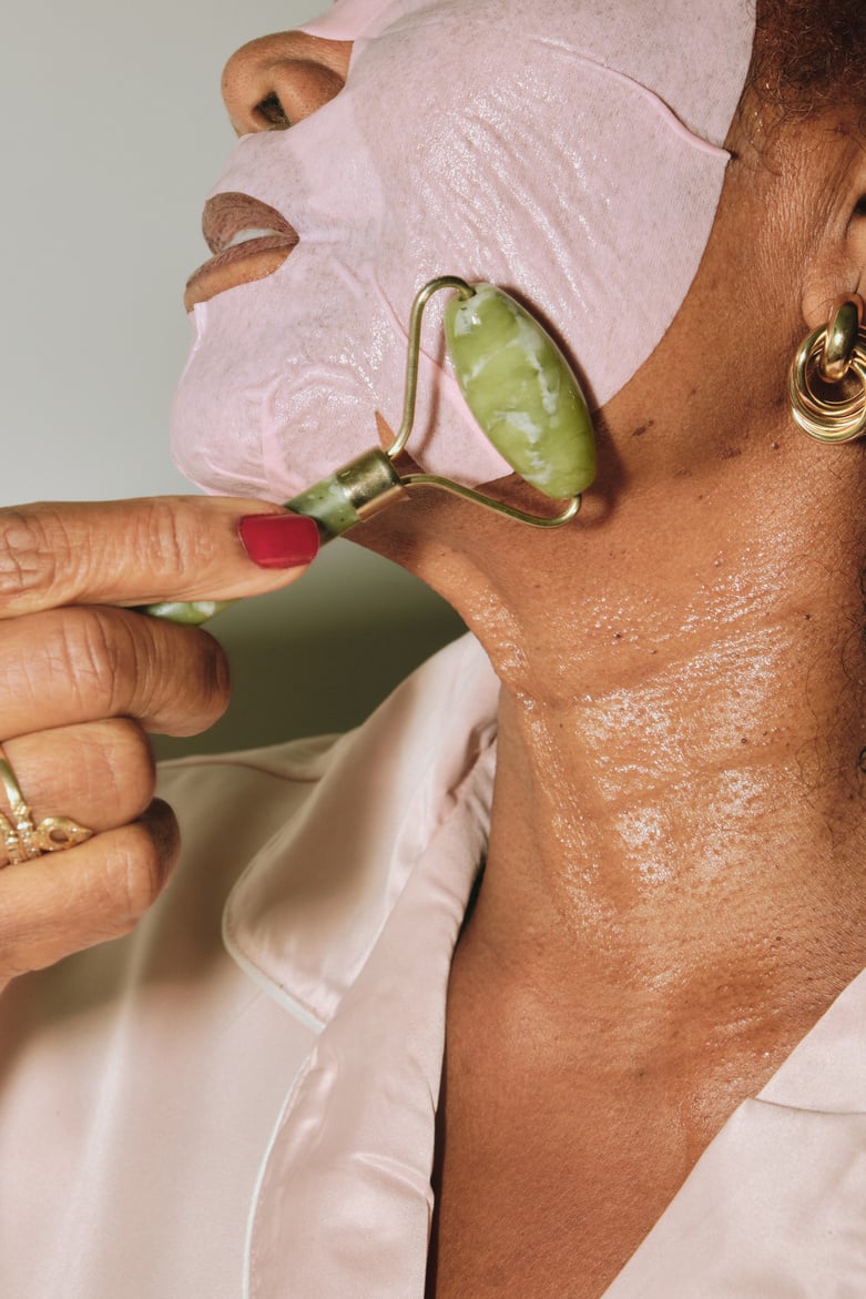 Woman with Facial Mask Using Jade Roller on Face